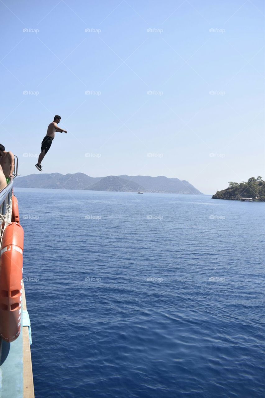 jumping into the sea from the highest part of a ship on a boat tour near fethiye turkey , islands in the background