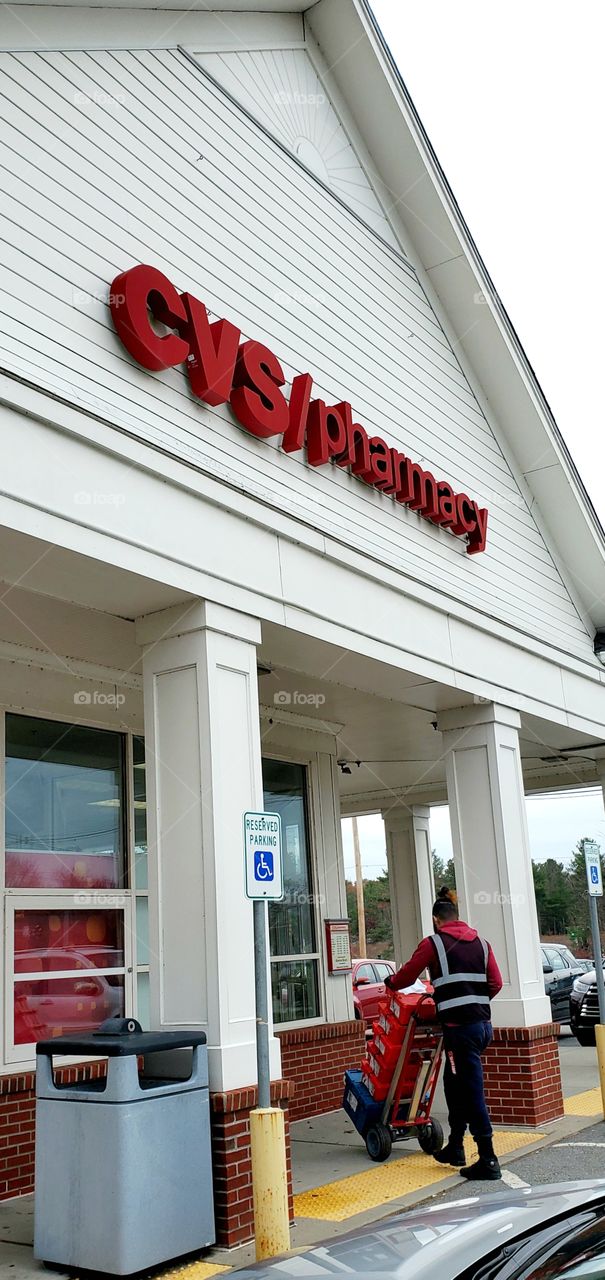CVS Pharmacy main entrance with handicapped parking sign in front. Delivery by man using 2 wheeler being made.