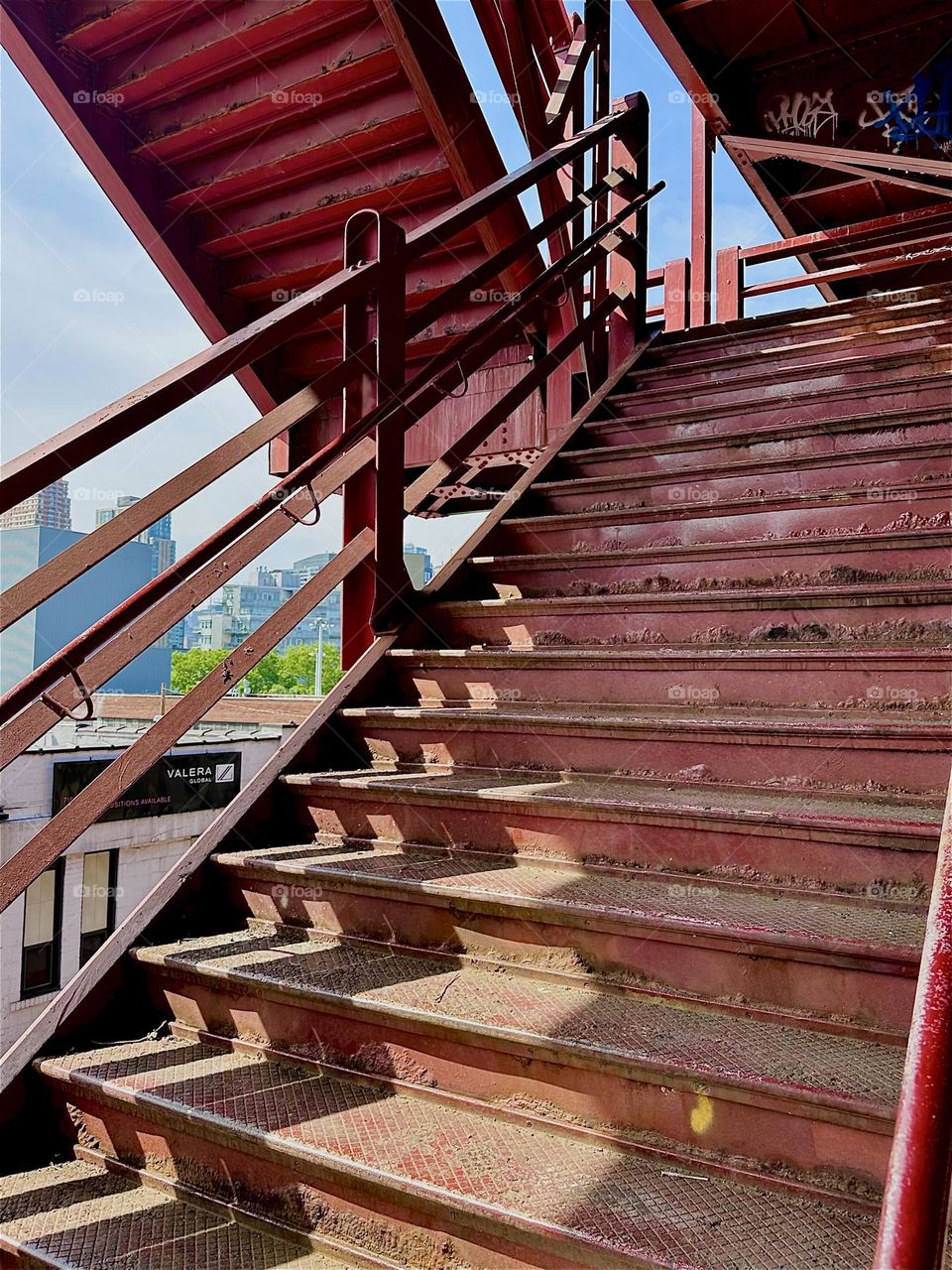 This is the red metal staircase of the “Pulaski Bridge” at “Newtown Creek” in LIC, Queens with its “Bauhaus” inspired industrial minimalist architecture. The afternoon sun casts intricate shadow patterns onto its surfaces. 2024. Hypnotic Productions