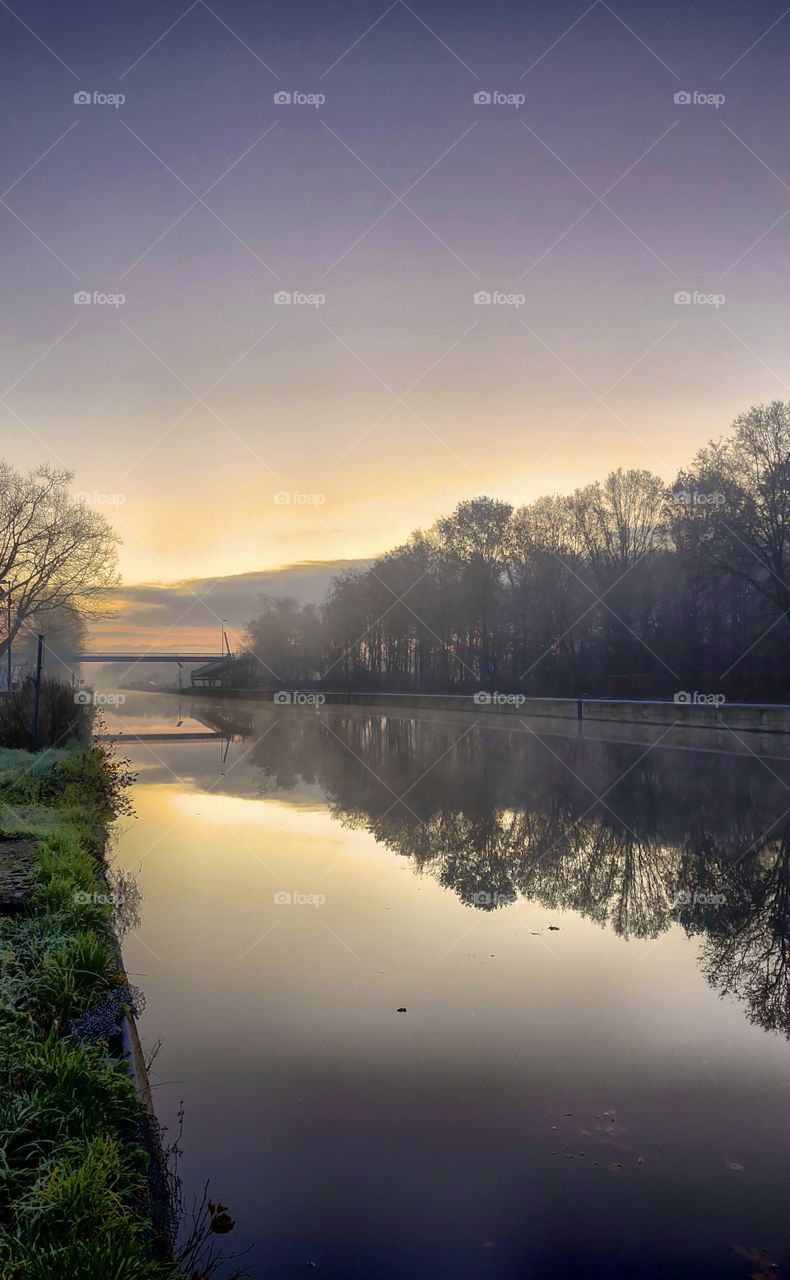 Soft winter sunrise reflected in the water of the river or canal