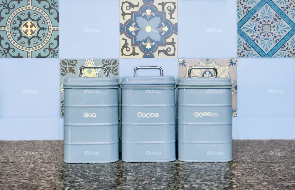 Blue kitchen storage tins against a tiled wall and on a granite worktop 