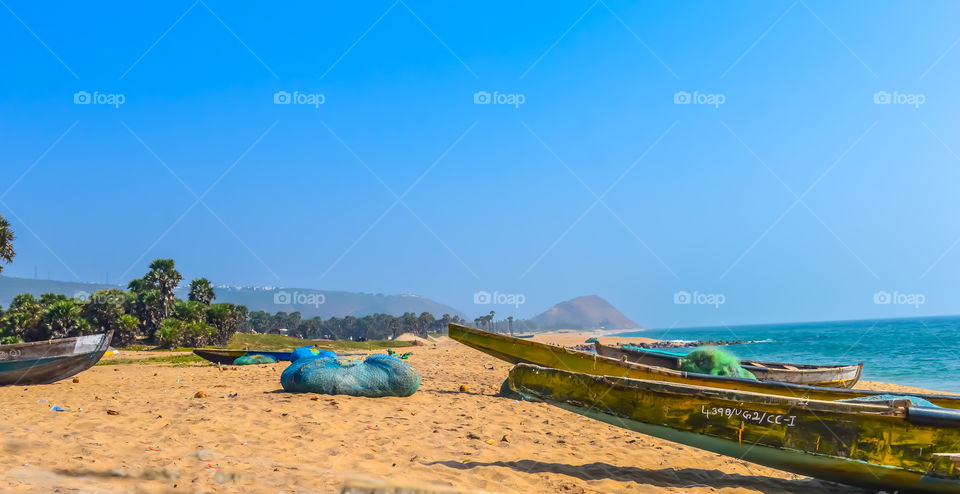 View of Fishing boats on beautiful sea shore at sunrise or sunset. Wild Empty Tropical beach, blue sky, yellow sand, sunlight reflections taken in landscape style may be used as a background, wallpaper, screen saver banner Travel vacation concept. Th