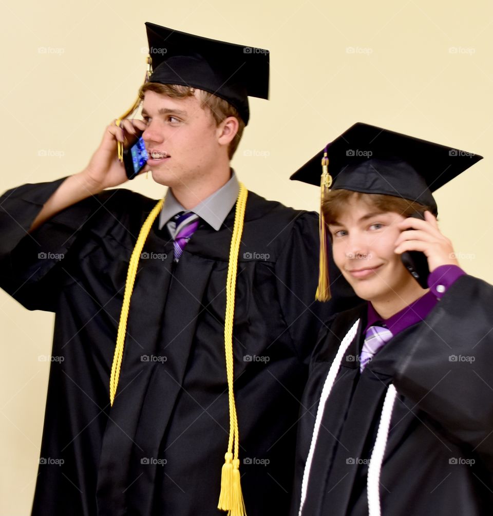 Two graduates talking on the cellphone before the graduation ceremony 