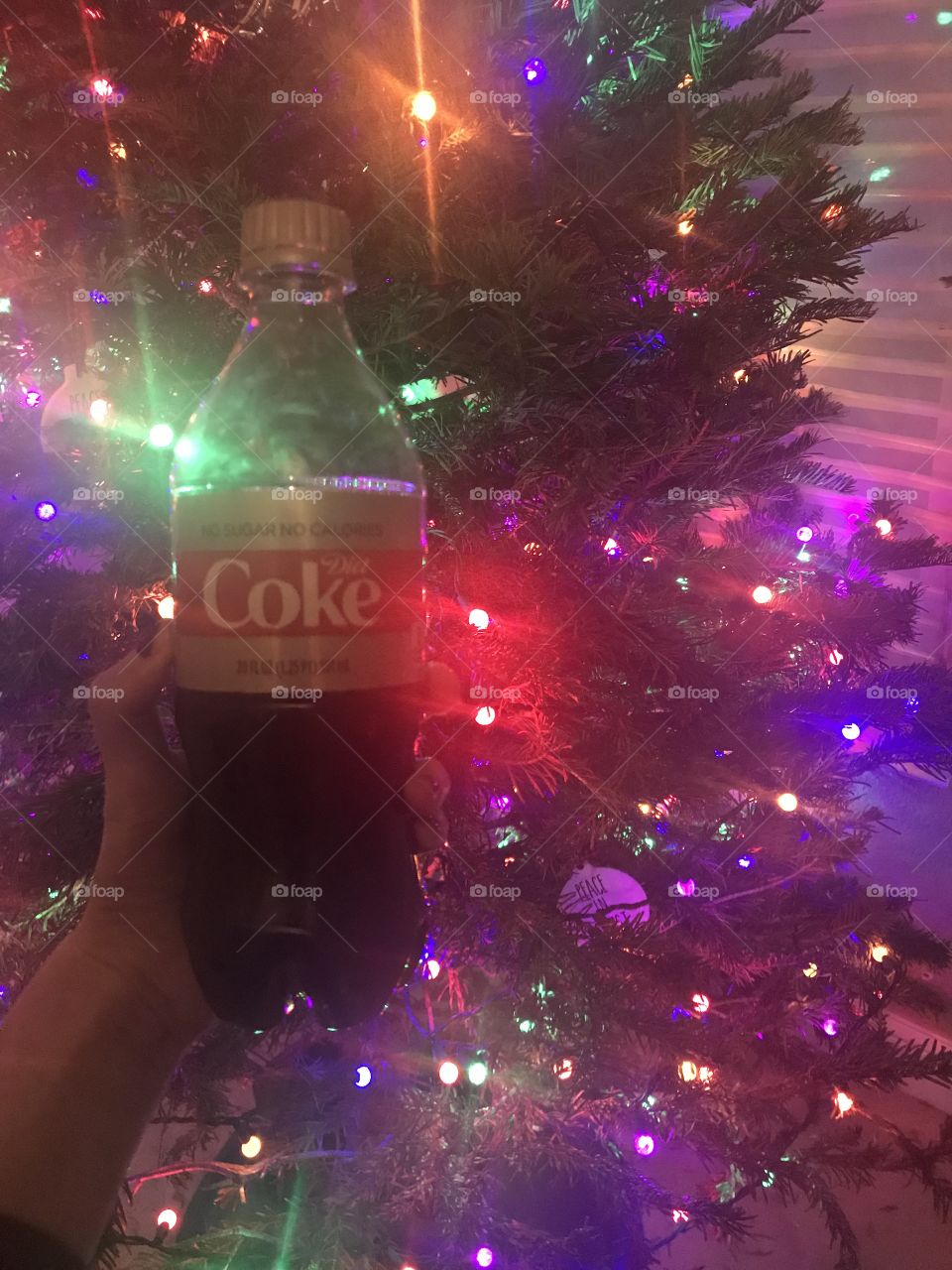 A woman holding a Diet Coke soda drink in front of a brightly lit Christmas tree. USA, America 