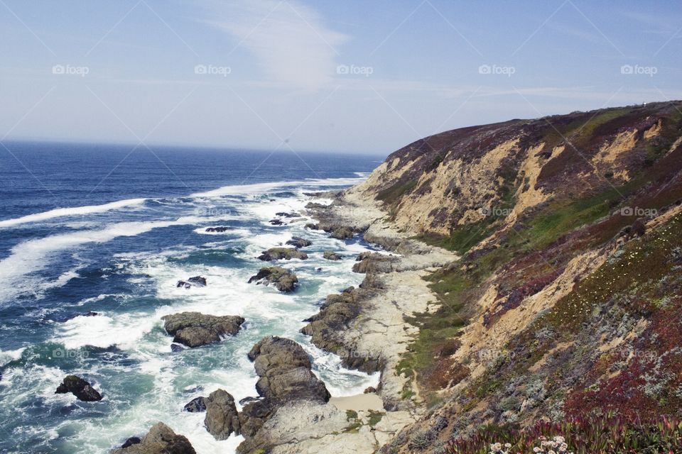 Sandy hill and a rocky shore by the bright blue sea in Half Moon Bay, California on a partially cloudy day