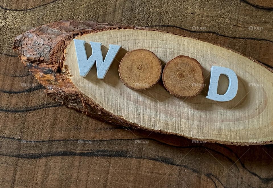 The word “Wood” spelt out in wooden letters on a live edge wood plaque against a wooden background 