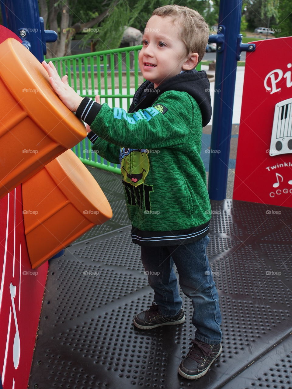 A little boy enthusiastically plays on the plastic drums on a play structure in the park. 