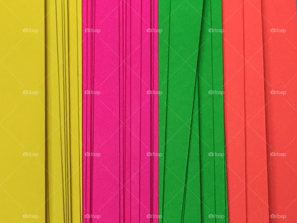Close up of a stack of neon colored paper. 