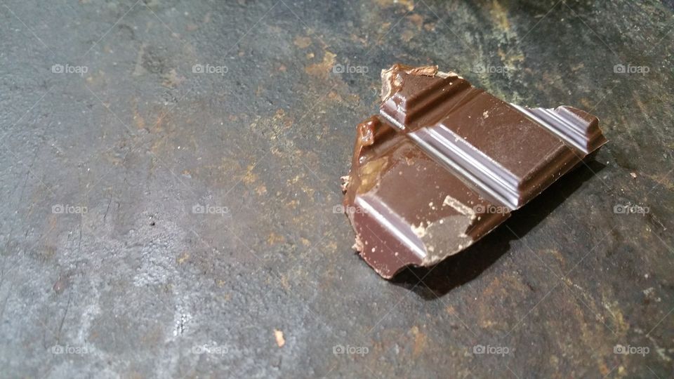 A piece of chocolate, half consumed, on rusty black surface