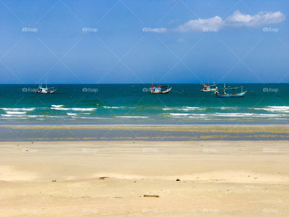 Fishing boats in turquoise sea at the sandy beach of Thailand 