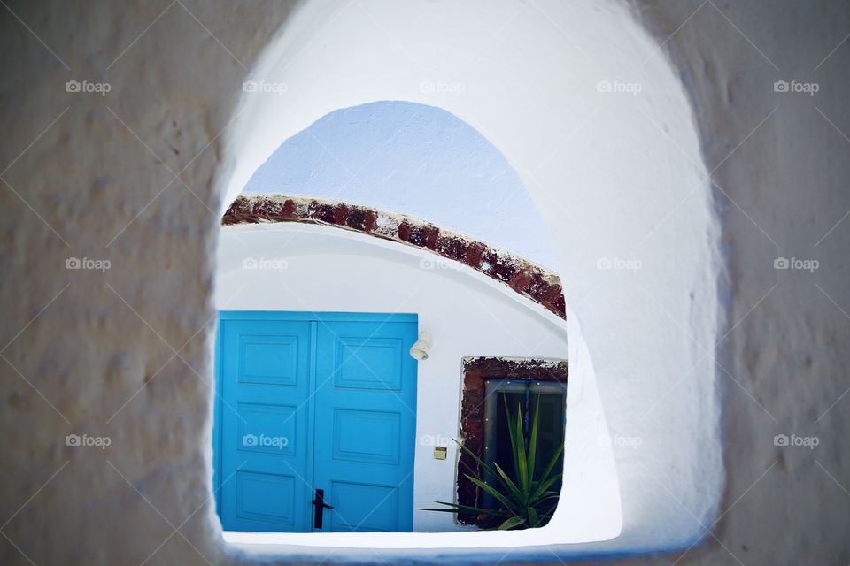 Looking through an old window in Greece against the street to a beautiful blue colored wooden door 