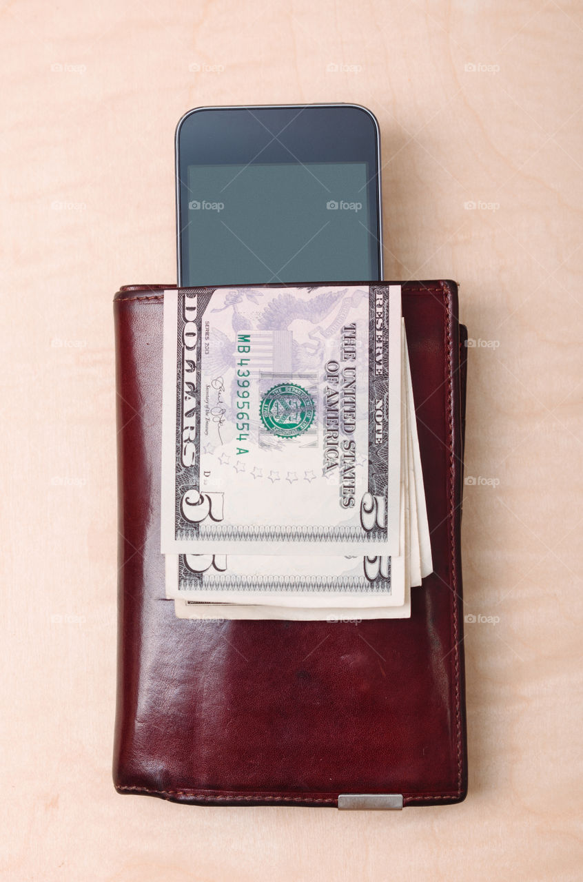 Wallet, smartphone with blank screen and dollar banknotes on wooden table. View from above. Portrait orientation