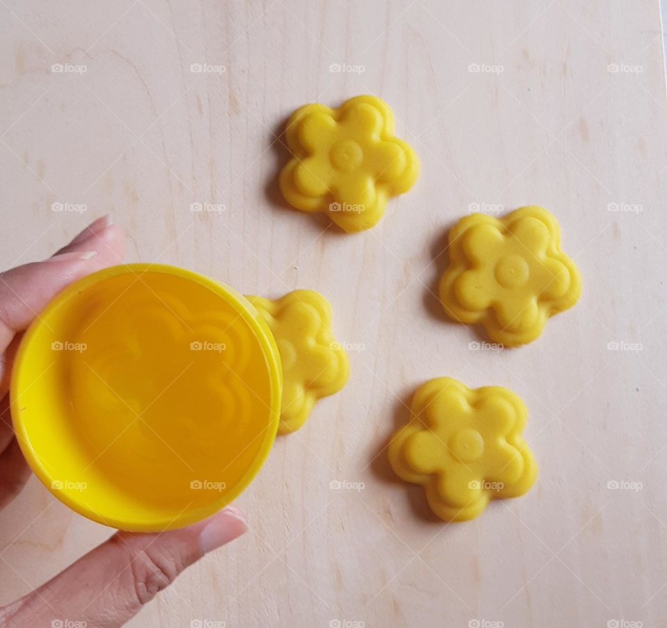 Yellow flowers shape of plasticine against wooden background, top view
