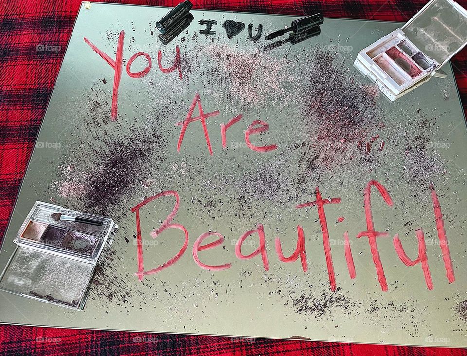 You are beautiful message written in lipstick, eyeshadows spilled on the mirror, intentional messages with makeup, makeup brands take a stand, reflections of makeup on a mirror, getting ready, punk style 