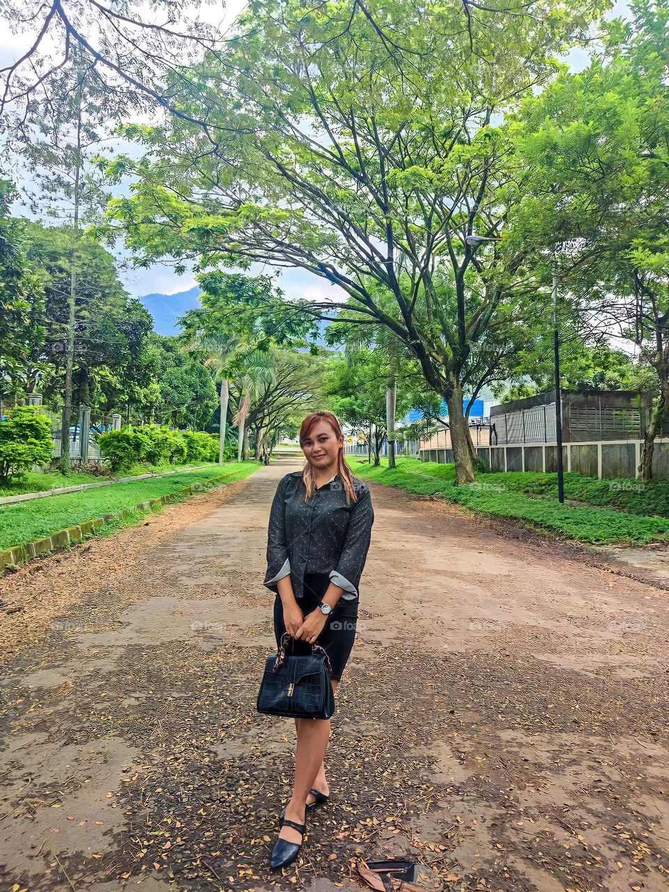 Portrait of a young woman standing looking at the camera carrying a bag in the middle of a shady and quiet street