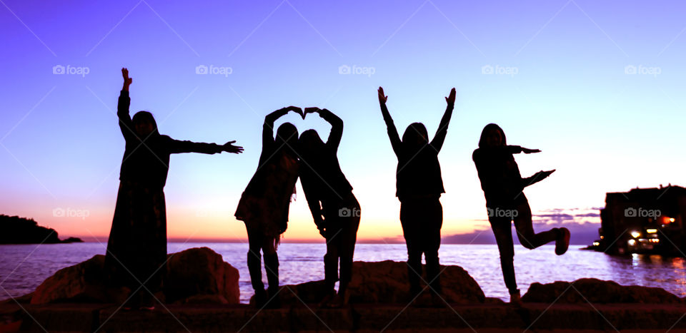 Silhouette of people making love sign by sea during sunset