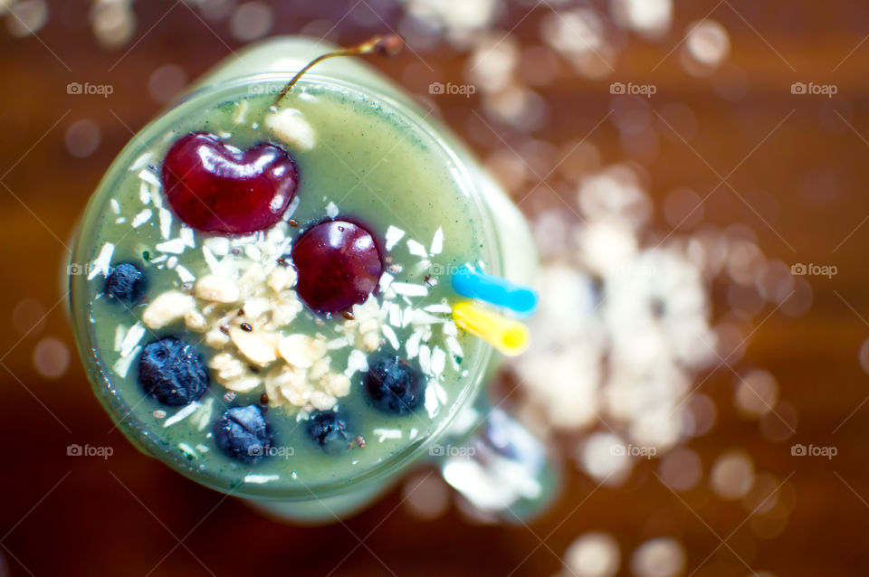 Green fruit smoothie with black cherries, coconut, granola and blueberry garnish in shape of smile high angle view feeling happy living a healthy lifestyle conceptual food photography background green fruit and spirulina or matcha theme