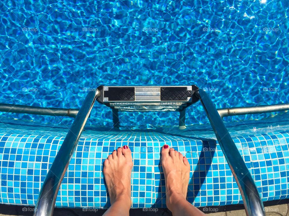 Woman's feet with red nails by the pool ready to get into the water