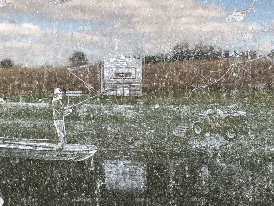 An engraved picture on a headstone at the cemetery. The landscape of a field and sky is reflecting off the headstone.
