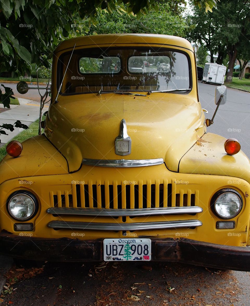 An old yellow International pickup with lots of chrome, sloped hood and strong grill parked on the streets of Bend in Central Oregon on a summer day. 