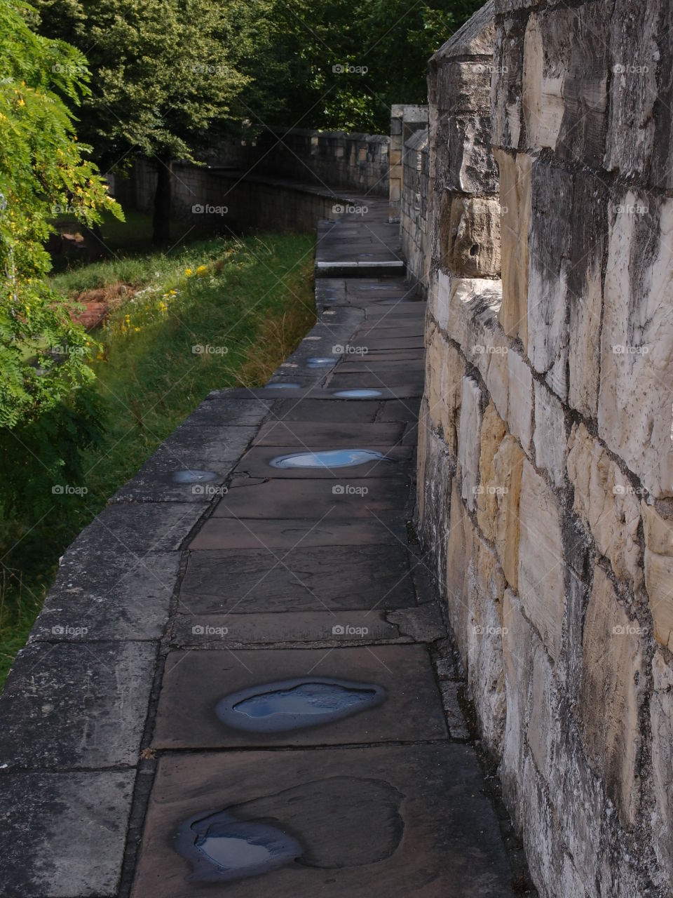 The stone path along the inside of the historic York Wall in England with the summer sun shining on small puddles of fresh rain. 