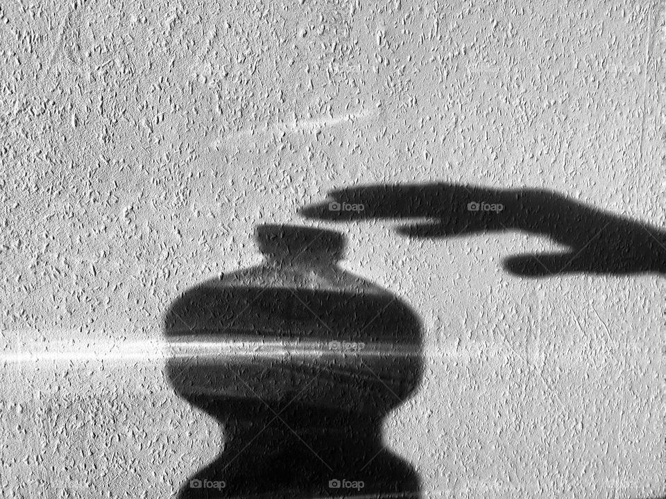 Silhouette of a bottle and a hand in front of a wall