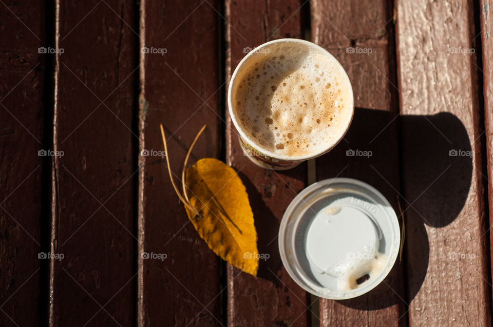 Morning take away coffee cup and yellow leave on wooden 