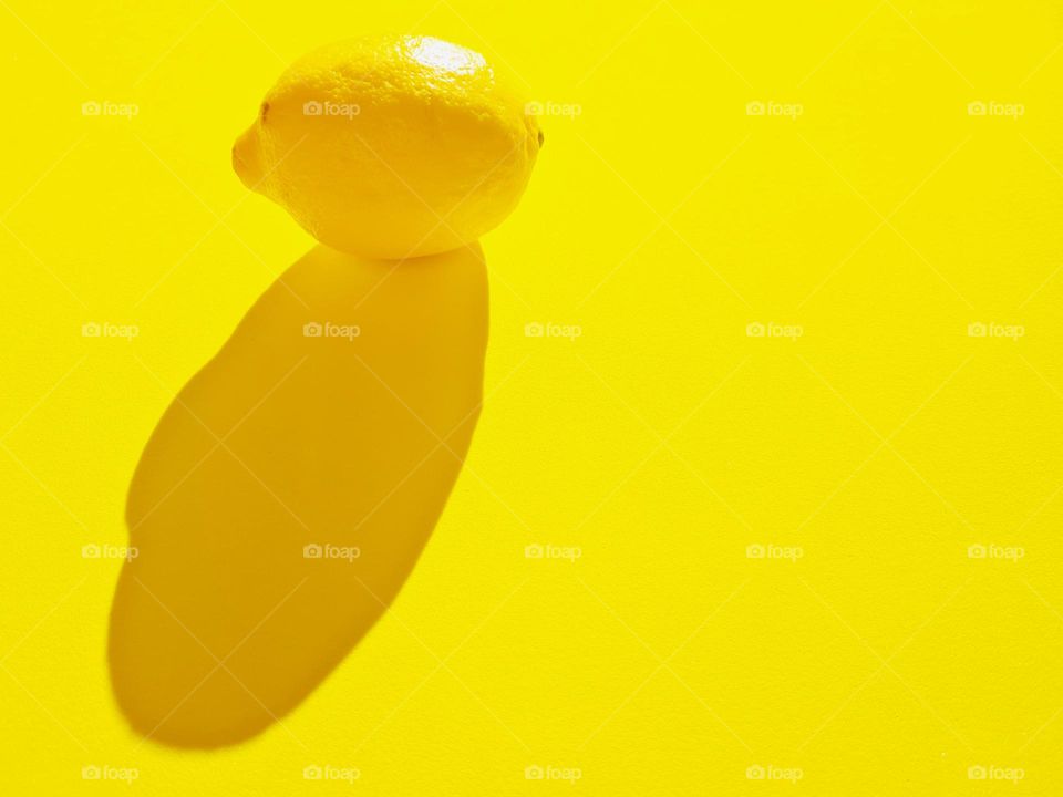 lemon and its shadow photographed on a yellow background