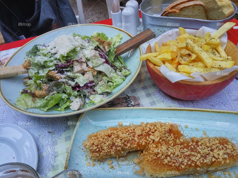 Greek food in Ioannina city, containing salad with lettuce toasted bread and chicken, Greek feta cheese in kantaifi with honey and almonds & fries