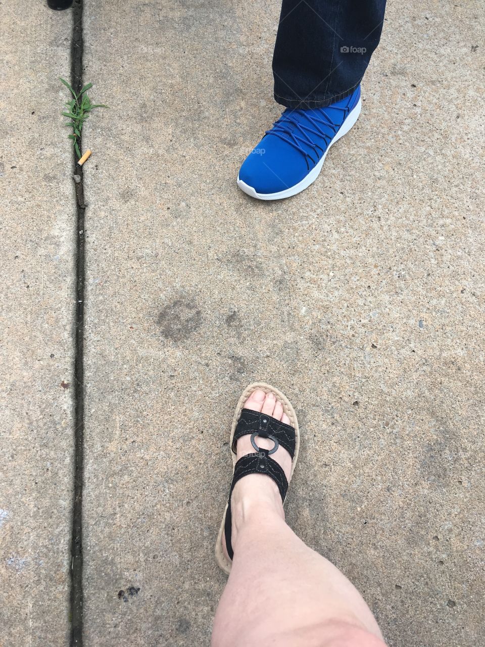 Standing around talking and taking pictures of two feet but not a pair....one woman ,one man 