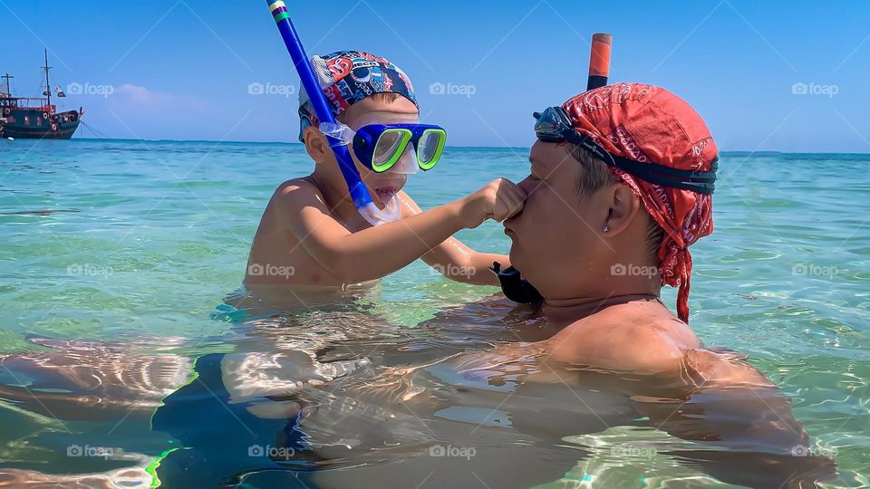 Father and son spend fun swimming in the sea with masks, sunny day