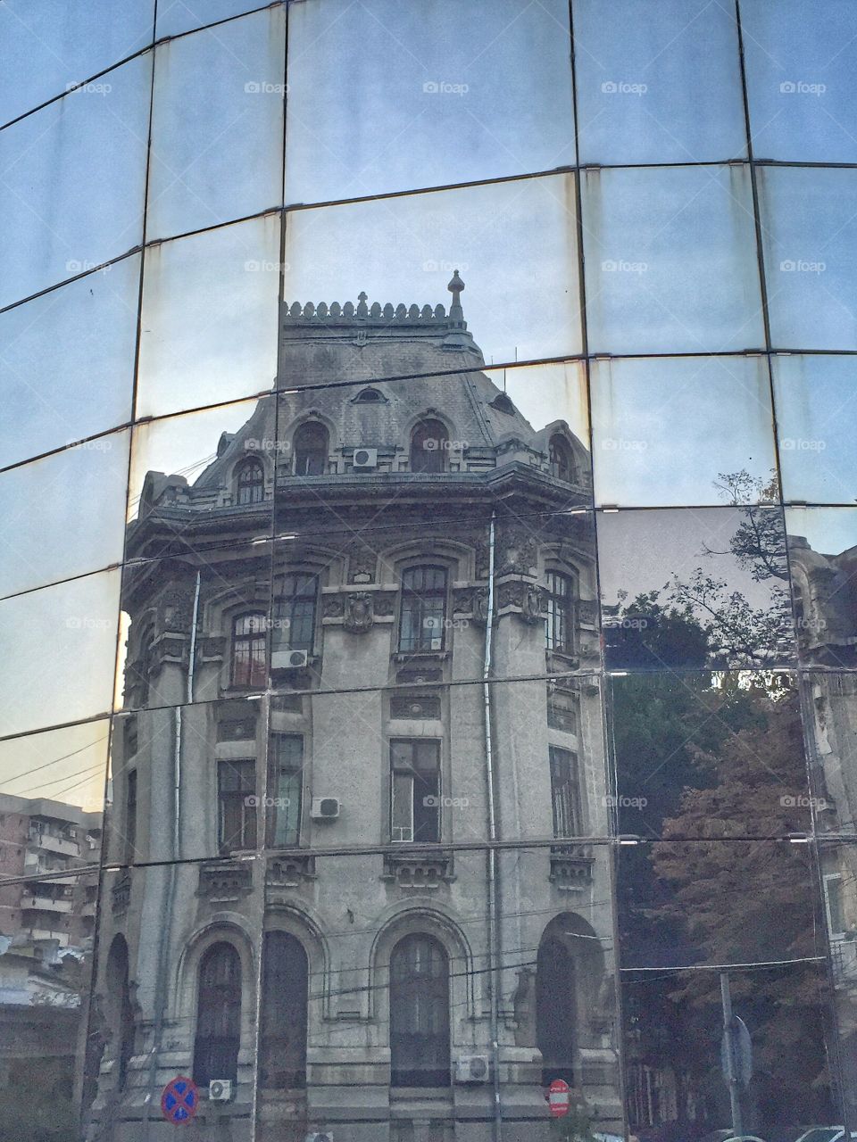 Old and new reflected . Reflection on a skyscraper facade of the Post's Custom building ( 1914/1926 Neo-Romanian style ) Bucharest, Romania