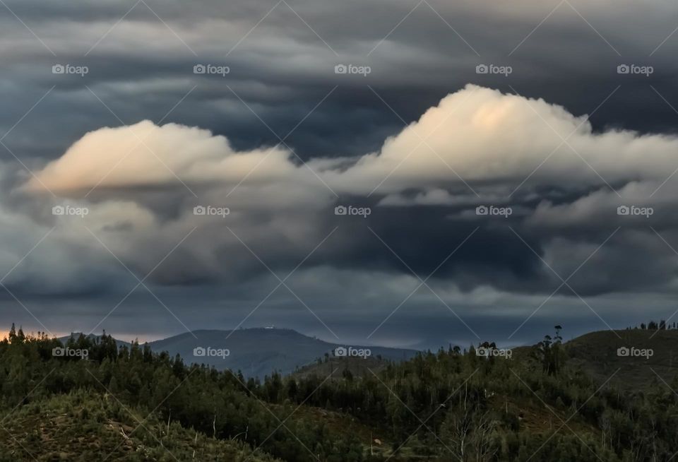 Dark clouds gather over tree covered hills around sunset