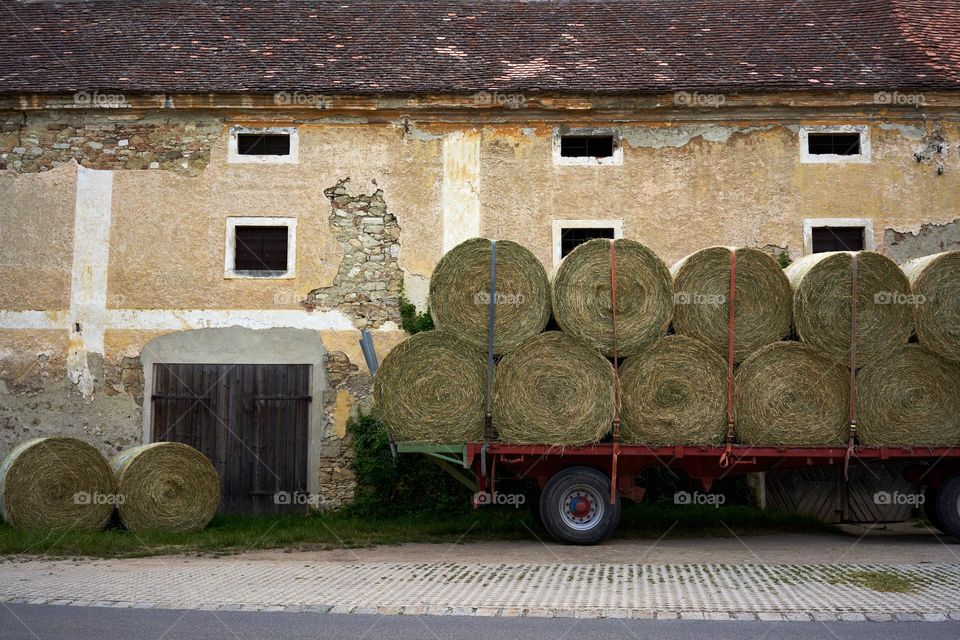 Circular hay bales on a trailer next to a barn