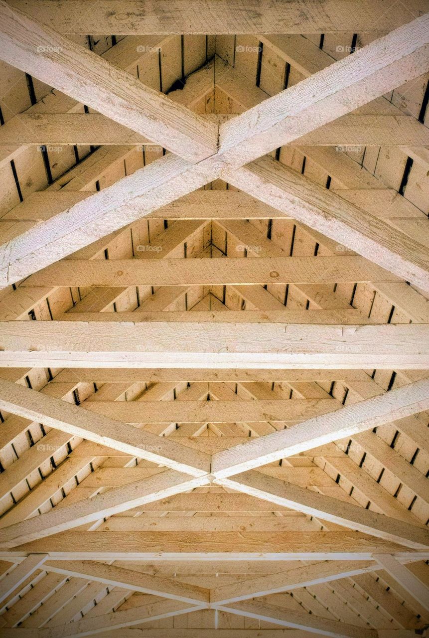 White wooden beams crossed to create the support for and ceiling of a rustic covered bridge in New England.