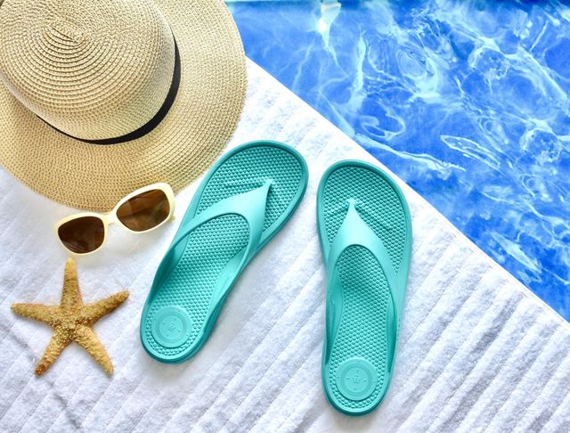 Poolside flat lay with sunglasses, flip flops, and a hat