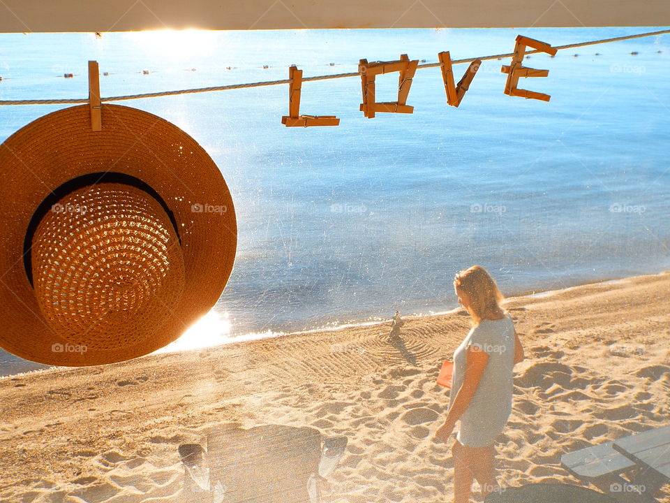 Women's straw hat on clothesline with letters LOVE spelled out with clothespins with beach and lake in background 