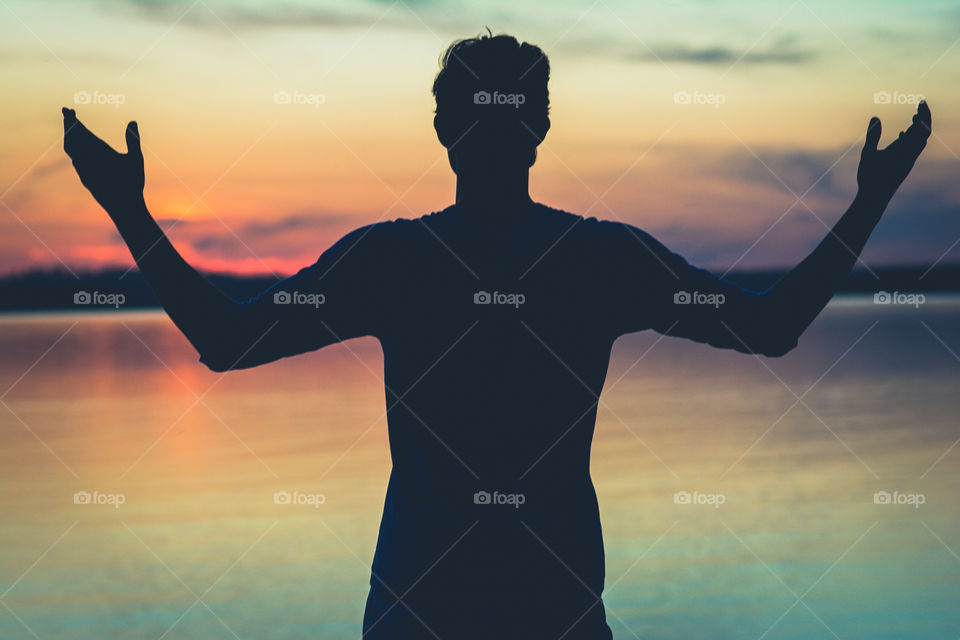 Silhouette of a Young Man Raising His Hands at the Waters Edge