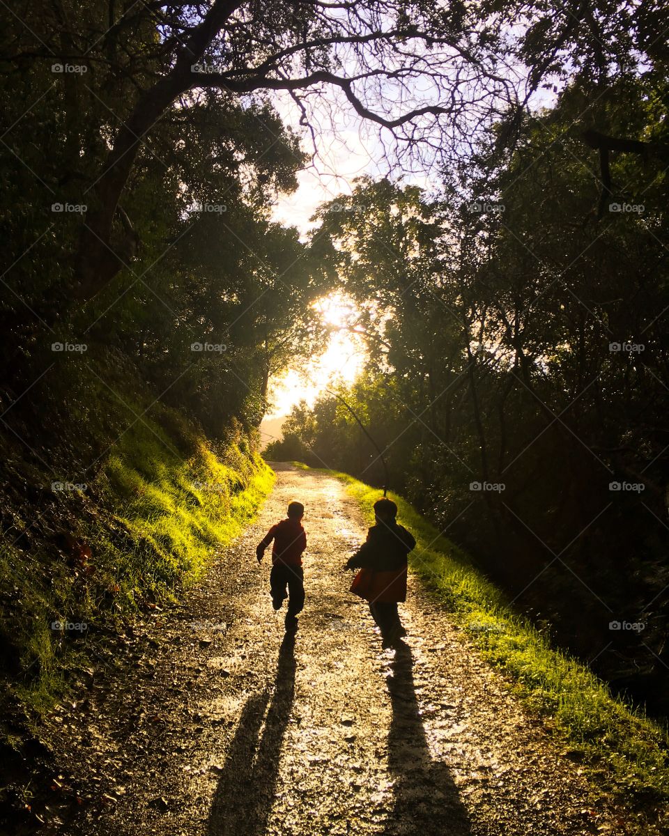 Two children run on a hiking trail with dramatic light behind creating silhouettes 
