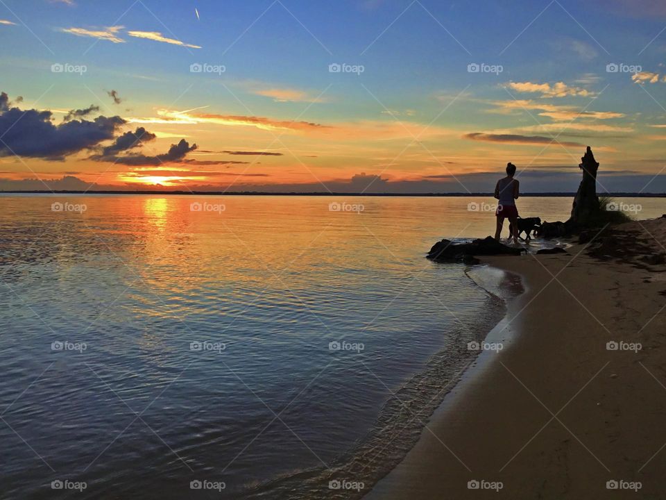 Woman walking her dog along the banks of the Choctahatchee bay during a magnificent sunset