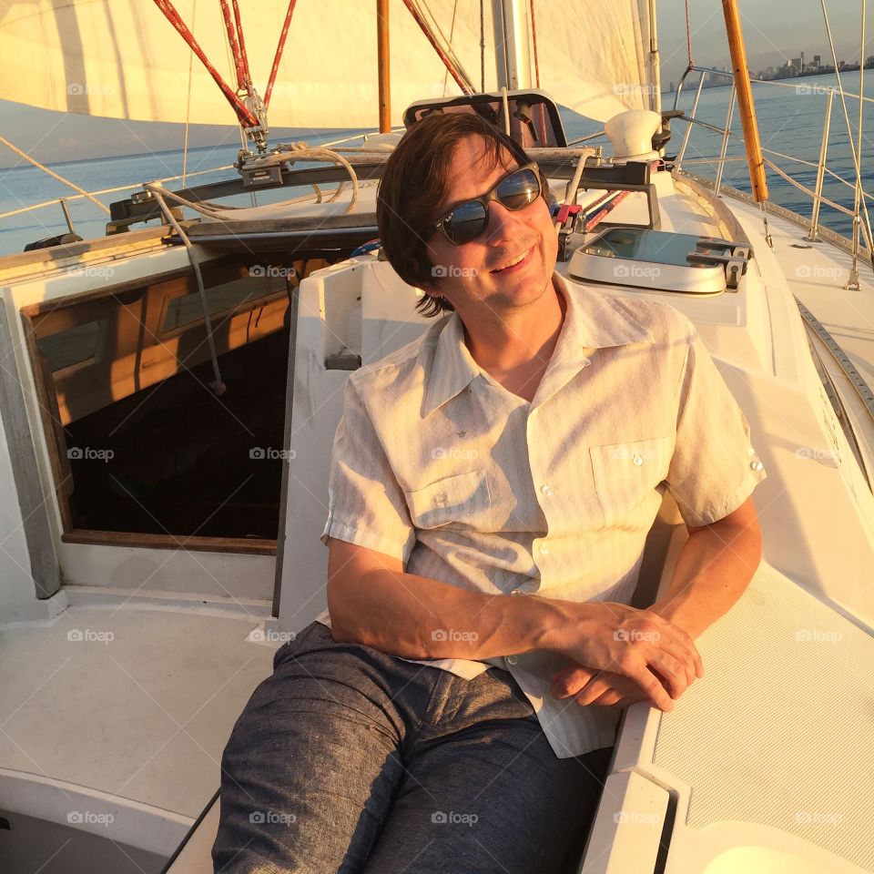 Sailing, 40 something, late afternoon, summer. Sailboat, water, wearing linen, sunglasses
