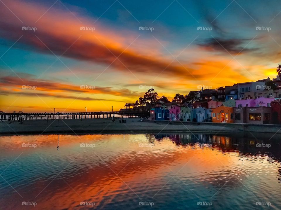 A beautiful sunset in Capitola California on the beach with the famous colorful Venetian condominiums with the reflection of the stunningly vibrant dusk sky on the Soquel River with the famous Capitola Wharf jutting out into the Monterey Bay 