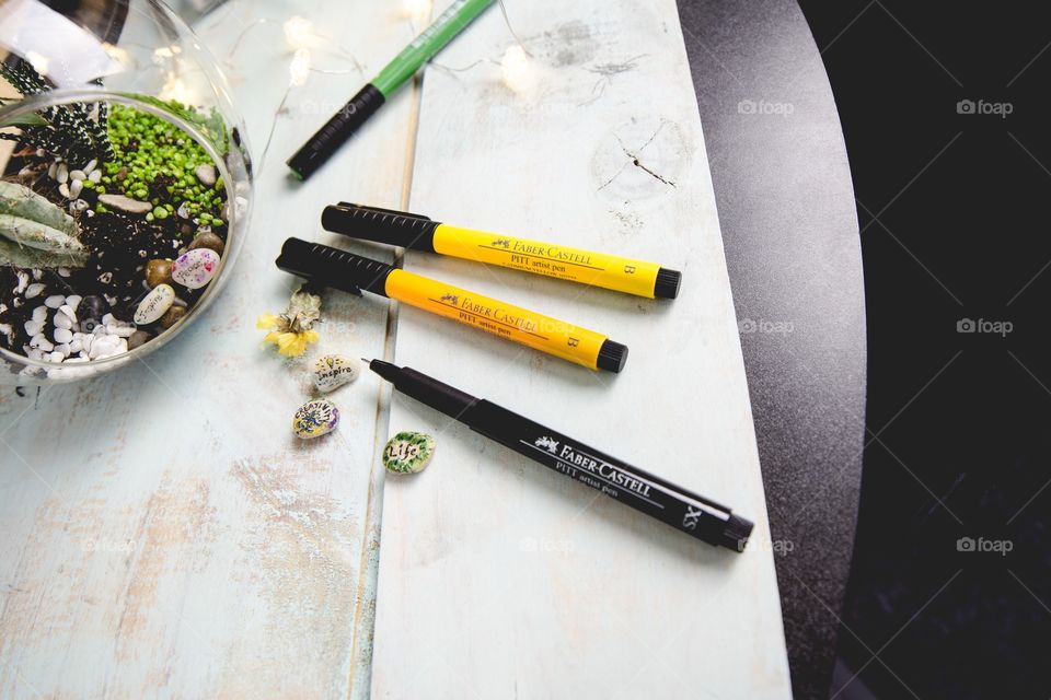 Succulents on glass dome with inspirational art stones make with Faber-Castell PITT Artist pens with words creativity, life, inspire and peace on rustic wood workspace conceptual tranquility and creative lifestyle photography