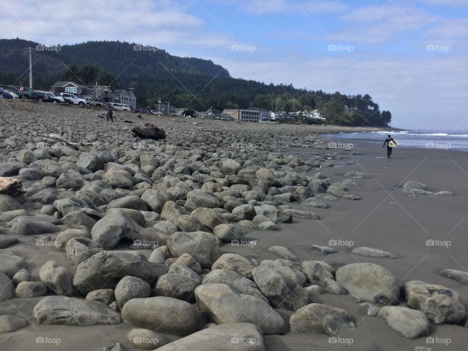 Rocks on the Beach with a surfer in the distance on the coast