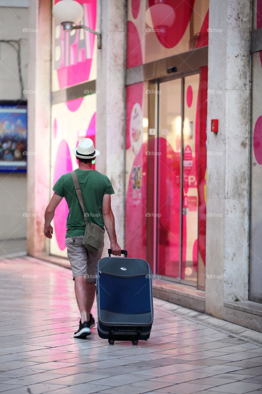 A tourist with a suitcase walking down the street when the light of shop windows