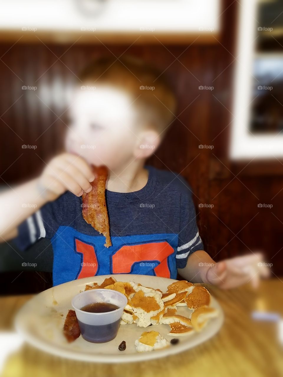 Young boy methodically dips bacon in syrup, anticipating the burst of flavors to come.