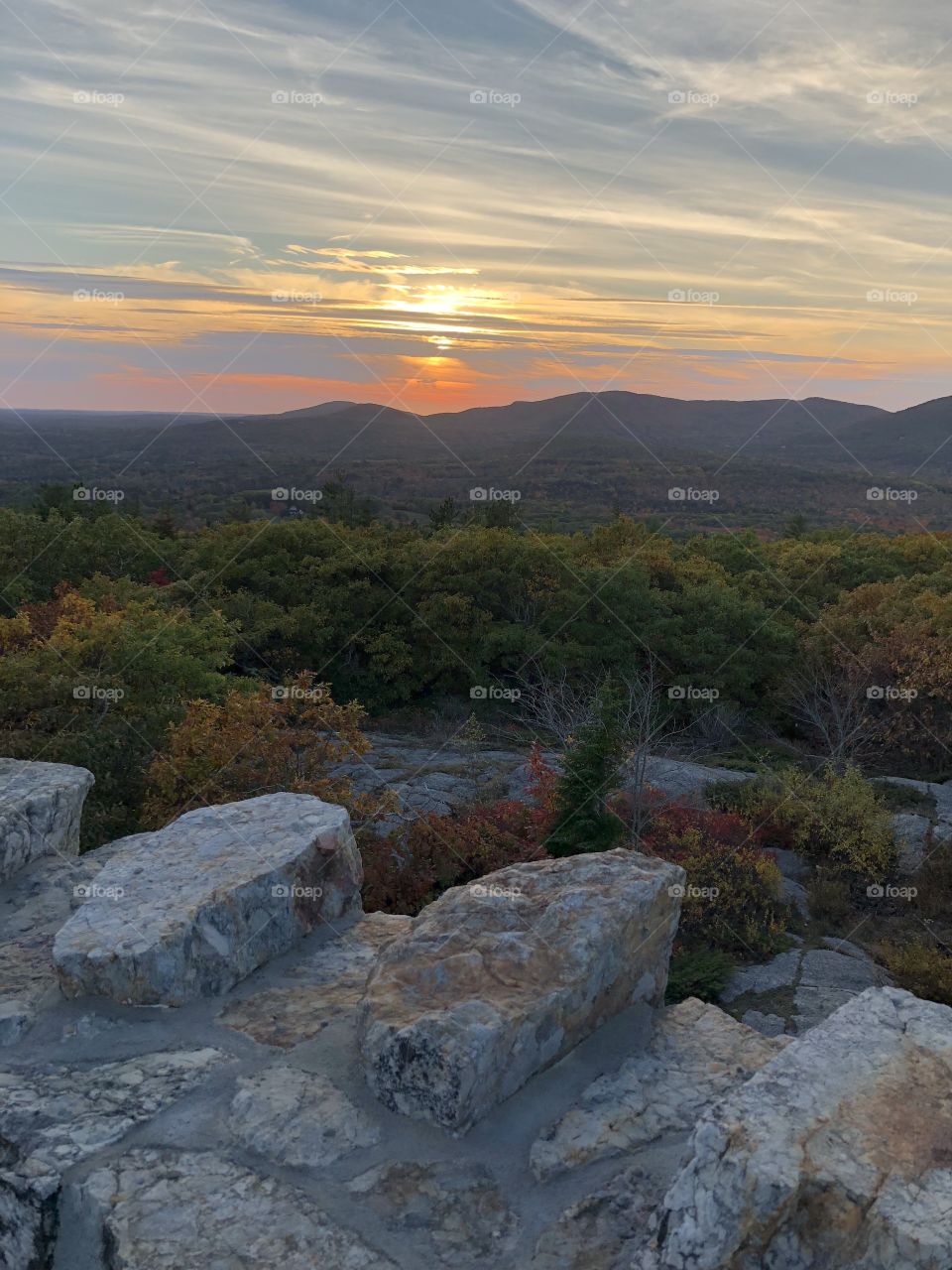 Scenic view of a late Autumn sunset over forested mountains from atop a stone lookout tower on the peak of Mount Battie in Camden, Maine 