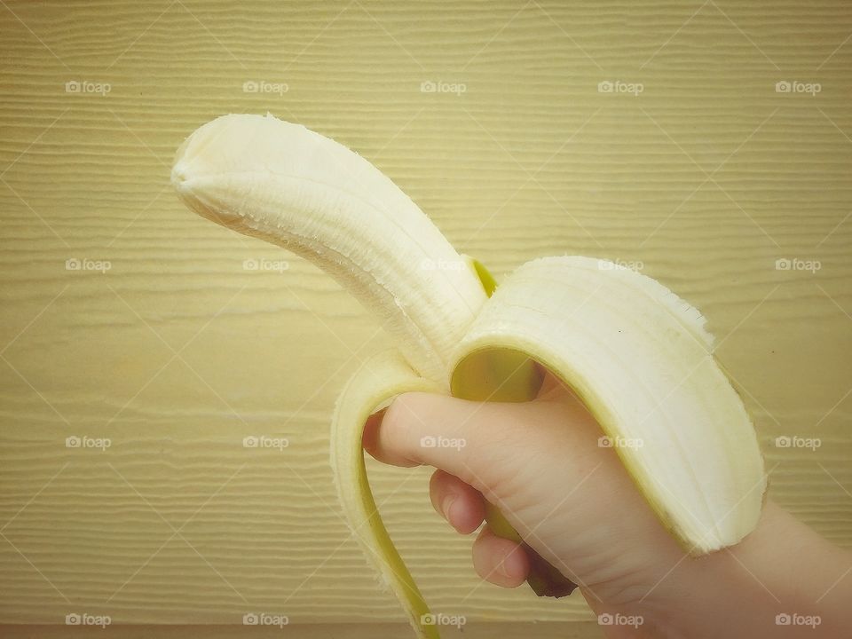 A hand holding a peeled banana on a yellow background