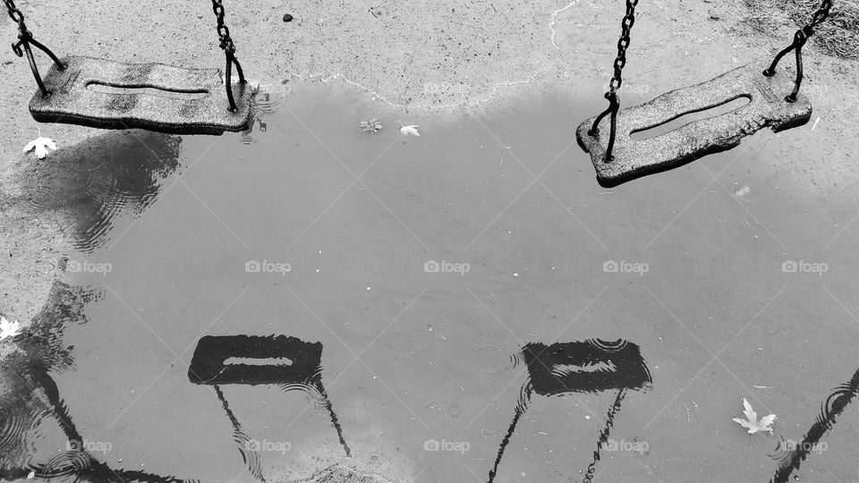 old chain children's swing in the reflection of a rain puddle