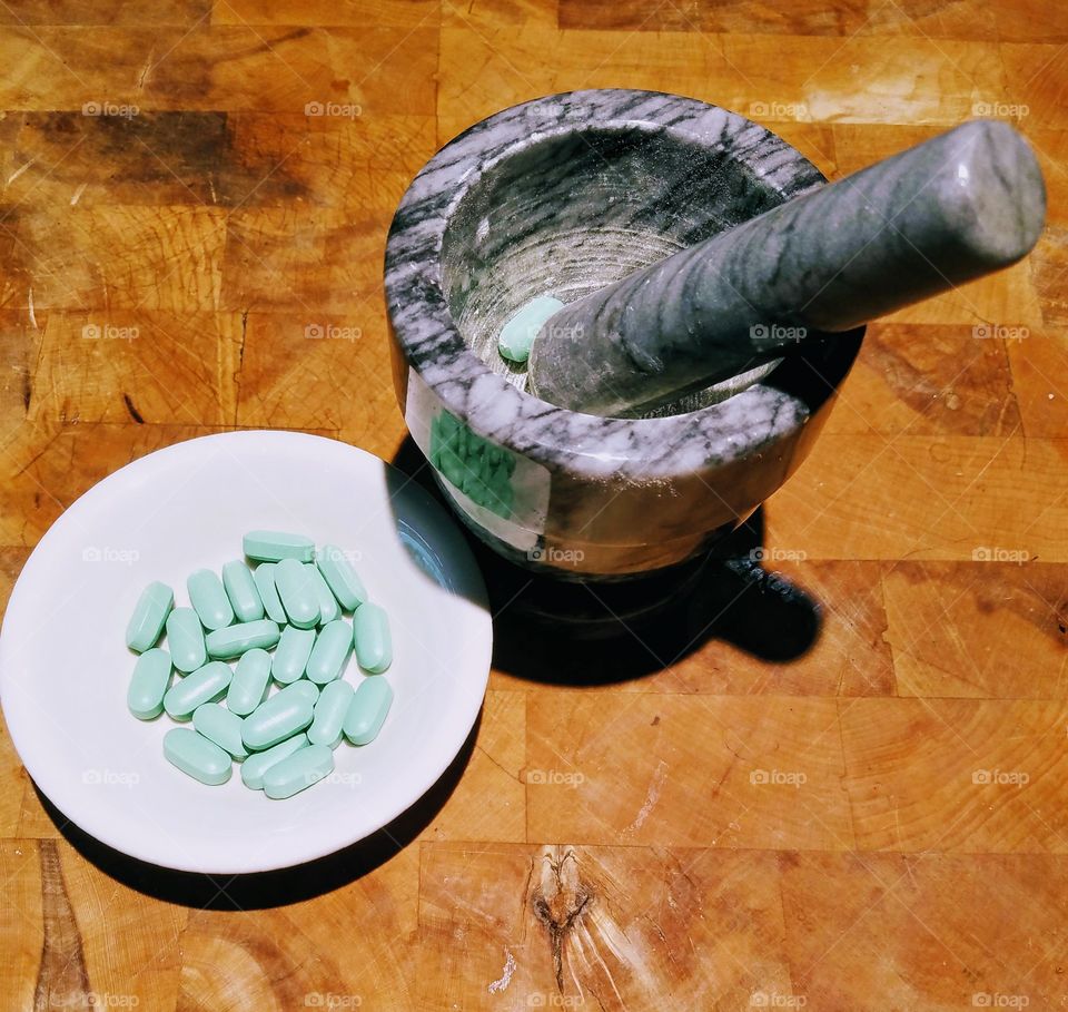 Crushing pills with mortar and pestle, made from marble. Crushing green pills into powder to put in food, drink or feeding tube.